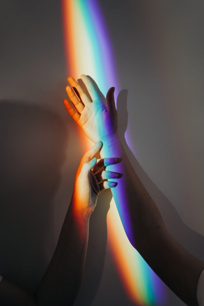 A beautiful display of rainbow light casting on intertwined hands symbolizing unity and love.